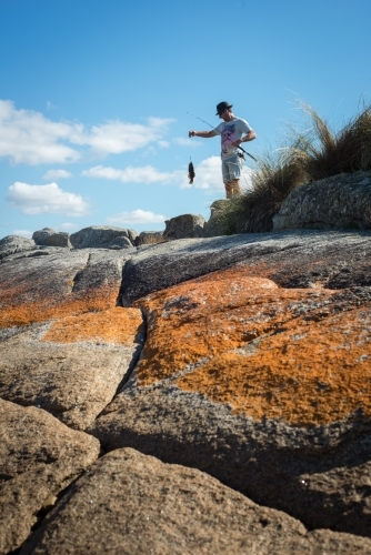 Man on boulder rocks at beach holding a fresh caught fish