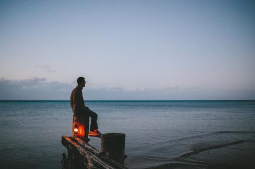 Man on old wooden jetty with lamp at dusk