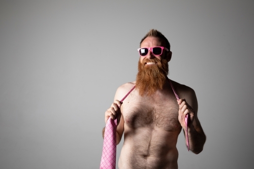 Man posing for photographs, shirtless with a pink tie and sunglasses - Australian Stock Image