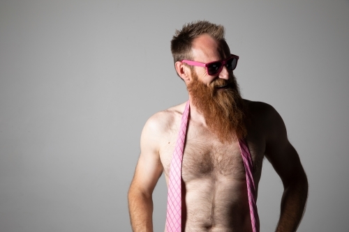 Man posing for photographs, shirtless with a pink tie and sunglasses - Australian Stock Image