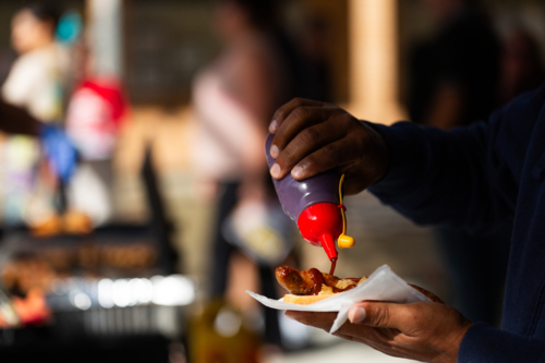 Man pouring bbq sauce at on sausage and bread held in hand on election day - Australian Stock Image