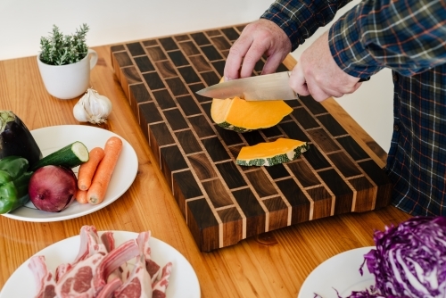 Man preparing lunch / dinner; cutting vegetables to cook with lamb cutlets - Australian Stock Image