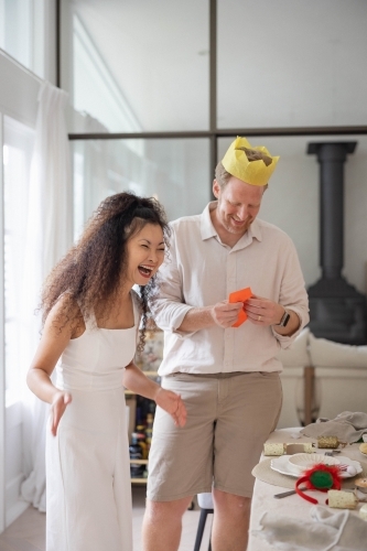 Man reading joke while woman laughs beside Christmas dinner table - Australian Stock Image