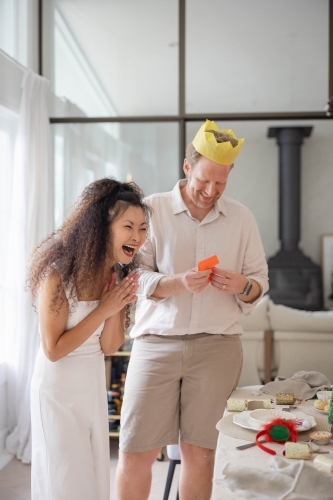 Man reading joke while woman laughs beside Christmas dinner table - Australian Stock Image