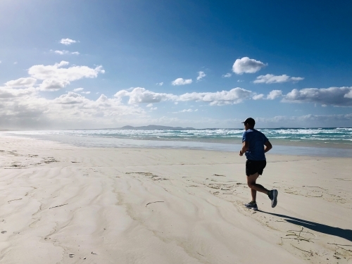 Man running on long white sandy stretch of beach