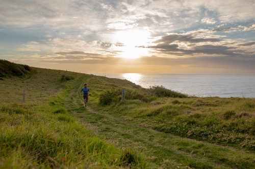 Man Running on winding lush, grassy field on the Coastside - Australian Stock Image