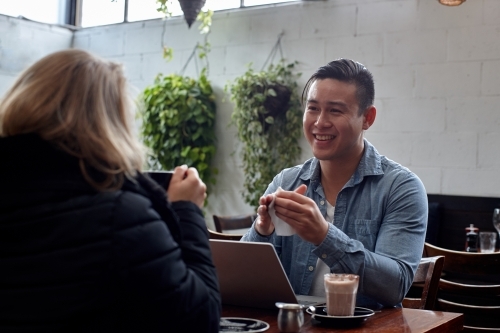 Man seated at table at cafe talking with friend - Australian Stock Image