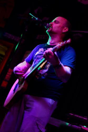 Man singing at microphone and playing accoustic guitar in purple lighting - Australian Stock Image