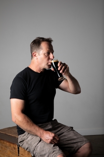 Man sitting, holding a glass of beer, relaxed and happy - Australian Stock Image