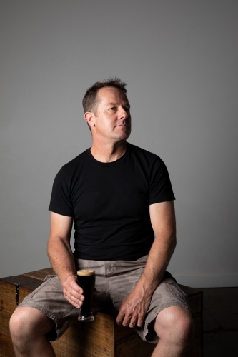 Man sitting, holding a glass of beer, relaxed and happy - Australian Stock Image