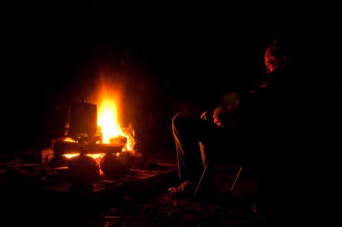 Man sitting in front of campfire boiling the billy at night - Australian Stock Image