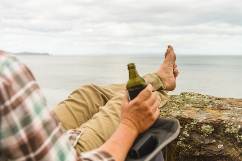 man sitting in tranquil camp spot by the ocean in his chair, with a beer