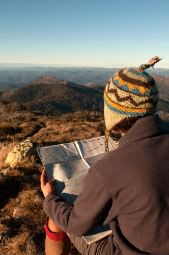 Man sitting on a rock overlooking mountain ranges, looking at a map. - Australian Stock Image