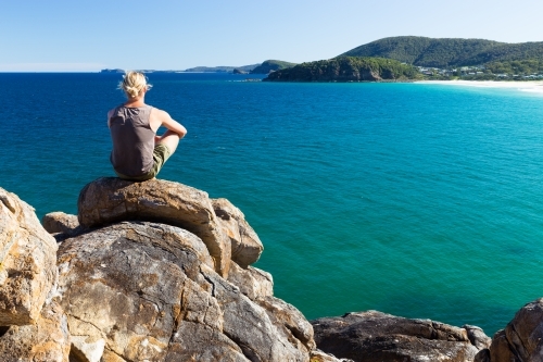Man sitting on a rocky headland looking out to sea - Australian Stock Image