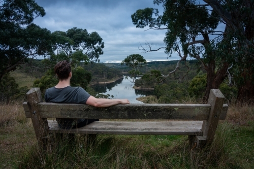 Man Sitting on Bench above a lake on a stormy afternoon