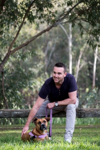 Man sitting on bench patting his dog in park - Australian Stock Image