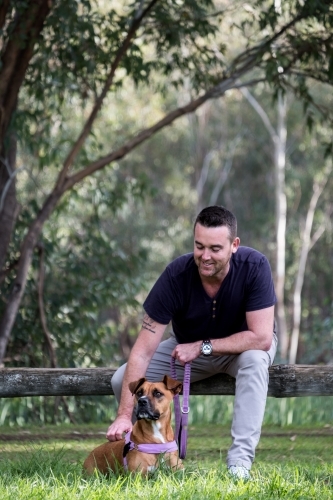 Man sitting on fence patting dog in park - Australian Stock Image
