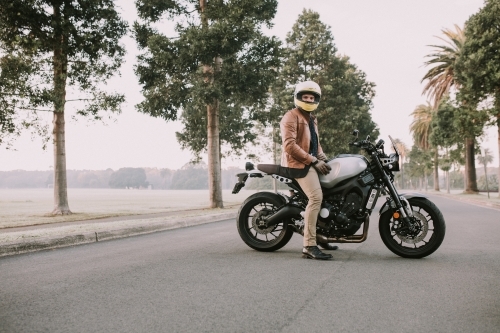 Man sitting on motorbike in middle of road at parklands - Australian Stock Image