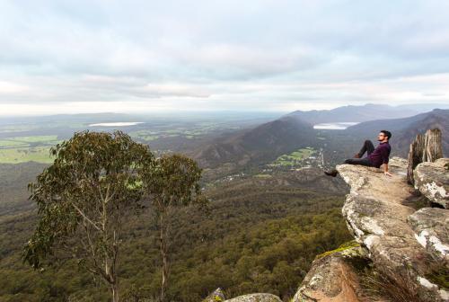 Man sitting on rocks looking out over landscape of green valleys - Australian Stock Image