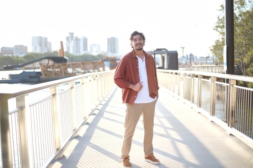 Man smiling on a pedestrian bridge with city background - Australian Stock Image