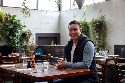 Man smiling sitting at table at restaurant - Australian Stock Image