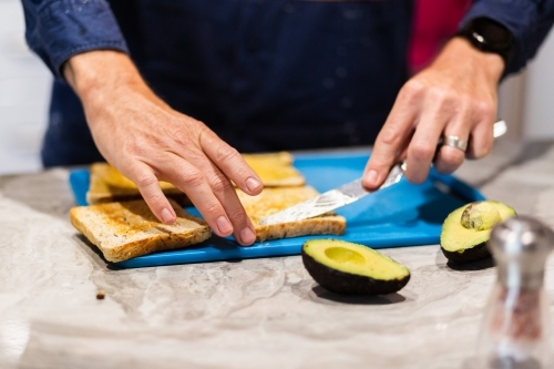 Man spreading butter on toast slice making his breakfast before work - Australian Stock Image