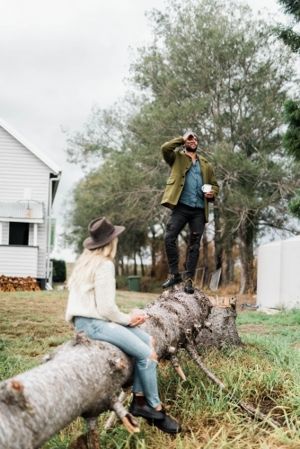 Man standing and woman sitting and drinking coffee on a fallen tree - Australian Stock Image