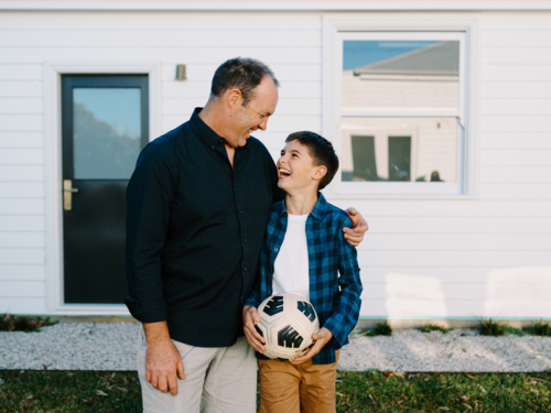 Man standing beside a young boy holding a soccer ball. - Australian Stock Image