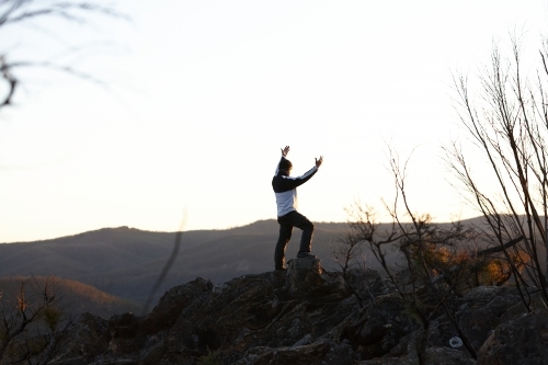 Man standing looking out over mountains on sunset - Australian Stock Image
