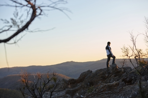 Man standing looking out over mountains on sunset - Australian Stock Image
