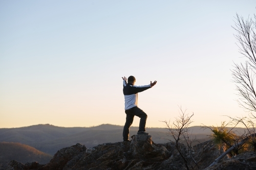 Man standing looking out over mountains on sunset - Australian Stock Image