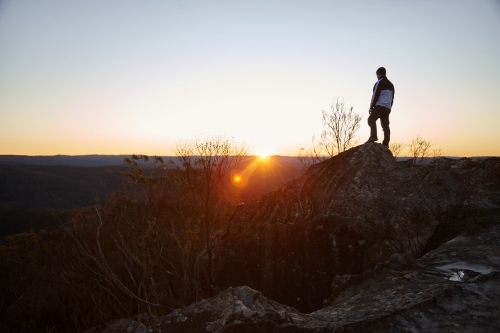 Man standing looking out over mountains on sunset - Australian Stock Image