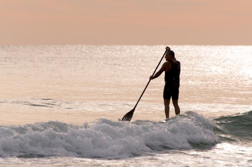 Man standing on paddleboard in pink dawn light - Australian Stock Image