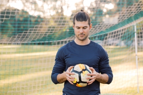 man standing on the field while looking down holding a soccer ball - Australian Stock Image