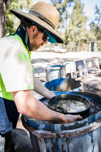 Man standing over fossicking drum of water with sieve - Australian Stock Image