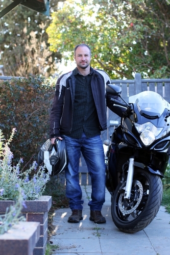 Man standing with motorbike in front of fence