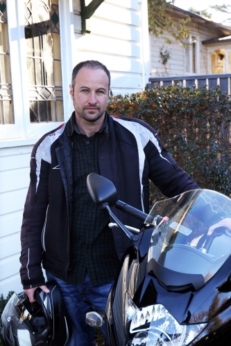 Man standing with motorbike outside of house - Australian Stock Image