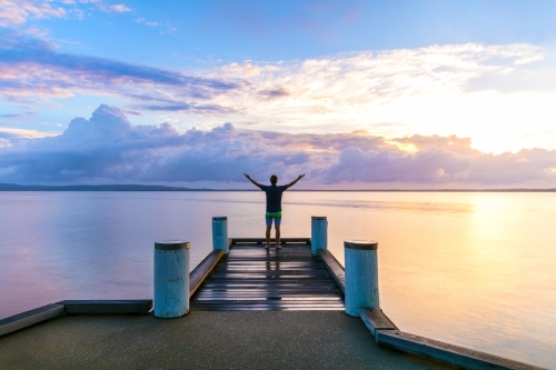 Man Standing With Outstretched Arms On A Jetty At Sunrise Man Standing With Outstretched Arms On A Jetty At Sunrise