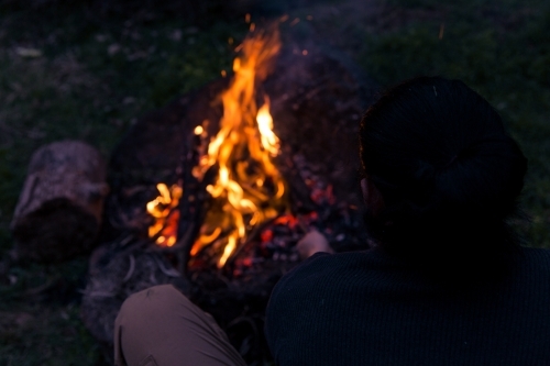 Man stoking roaring camp fire at night - Australian Stock Image