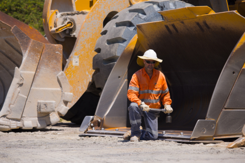 Man tightening the bolts on the bucket of a payloader. - Australian Stock Image