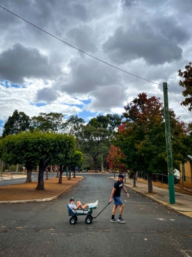 Man towing young boy with broken leg in cart across deserted road with autumn trees in background