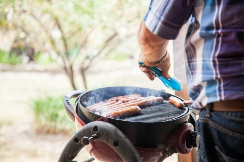 Man turning snags on a backyard barbie - Australian Stock Image