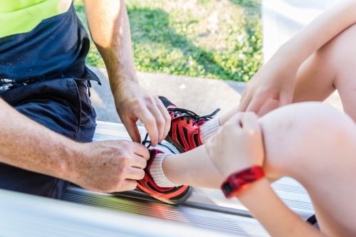 Man tying shoelaces on shoes of child - Australian Stock Image