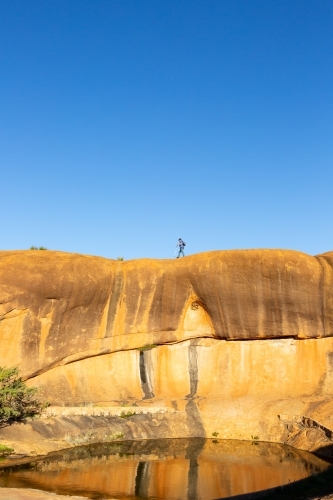 man walking across rock above a natural pool of water - Australian Stock Image