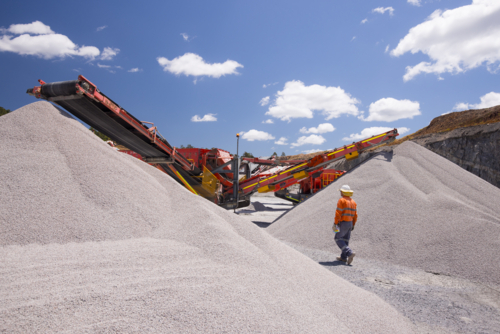 Man walking in between piles of aggregates near the crusher. - Australian Stock Image