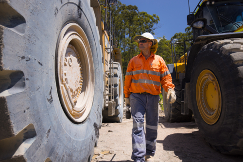 Man walking in between the massive wheels of payloader dump trucks - Australian Stock Image