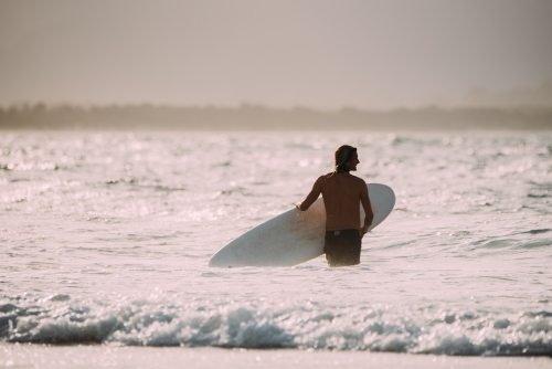 Man walking into the surf at sunset - Australian Stock Image