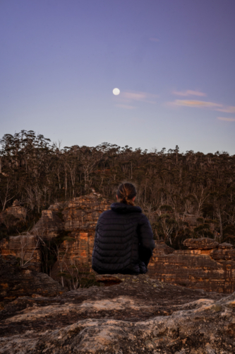 Man watching moon sitting on mountain cliff - Australian Stock Image