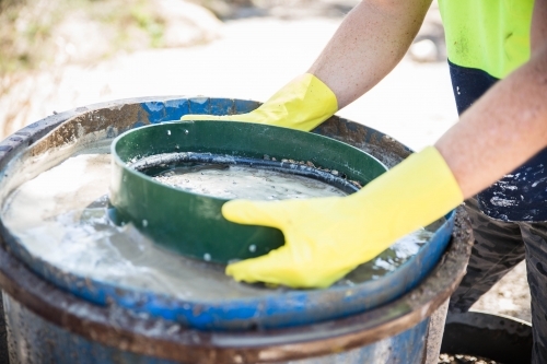 Man wearing gloves standing over fossicking drum of water with sieve - Australian Stock Image