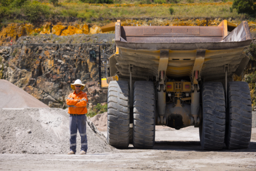 Man with arms crossed standing behind the hauler truck with massive wheels. - Australian Stock Image